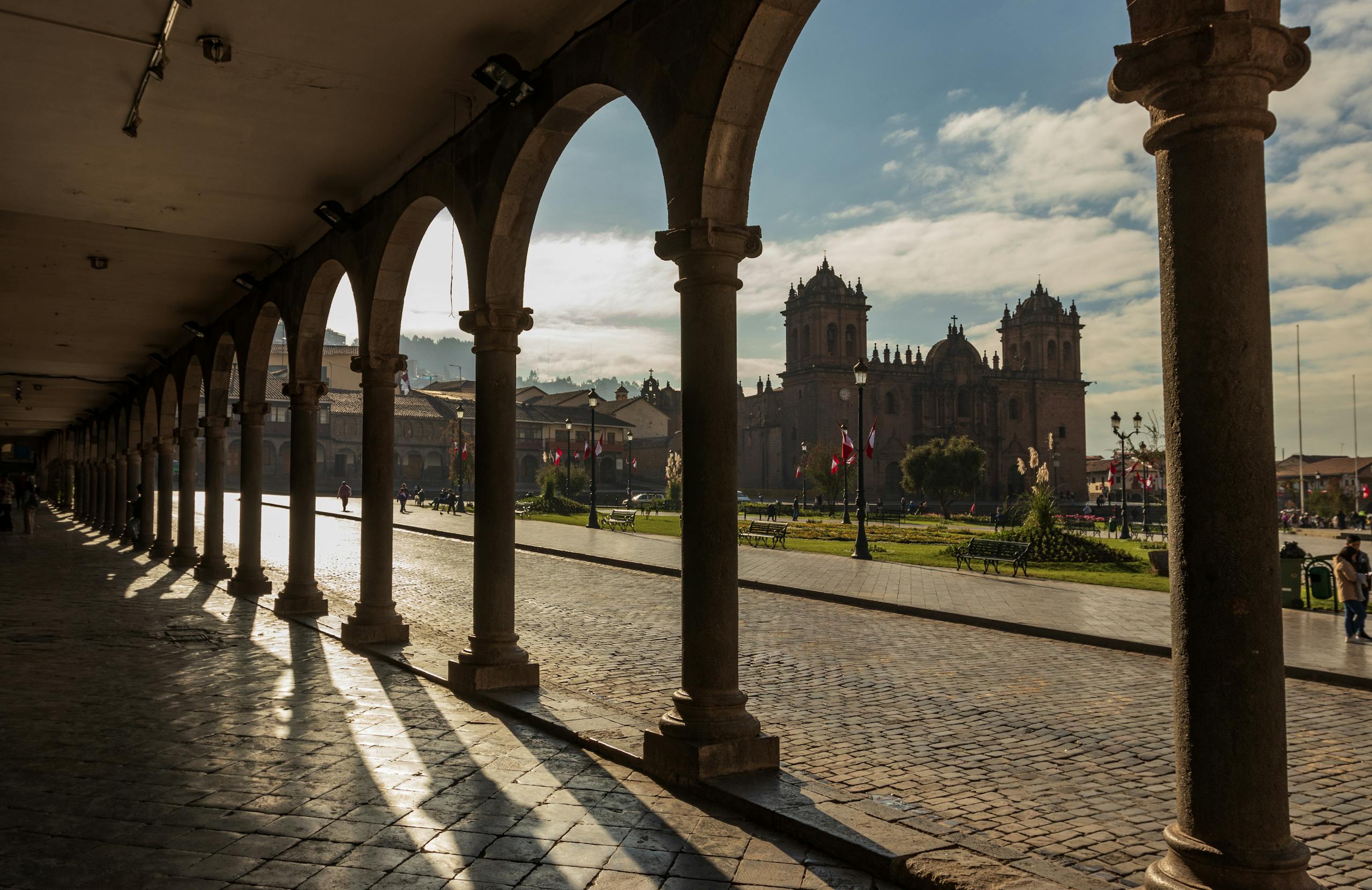 Dramatic shadows cast by colonnades in Cusco, Peru, framing a historic cathedral.