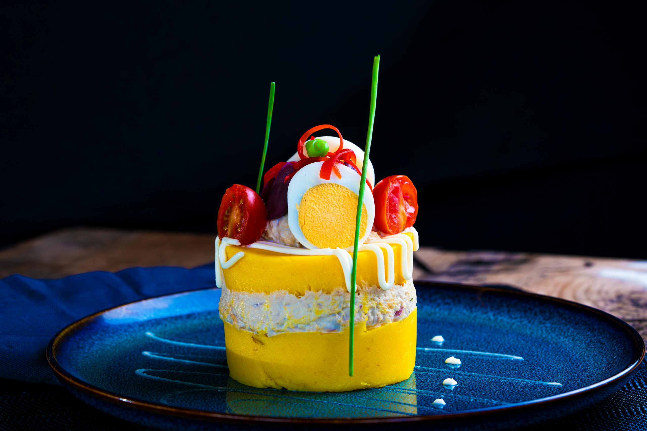 Vibrant Peruvian Causa Rellena with artistic presentation on a blue plate.